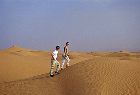 Young man and woman walk up sand dunes in the Sahara Desert, Morocco